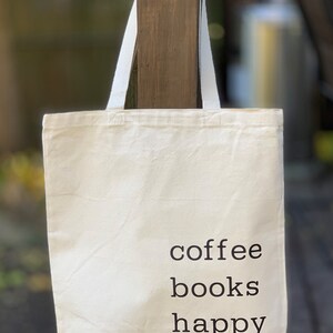 May include: A white canvas tote bag with black text that reads "coffee books happy".