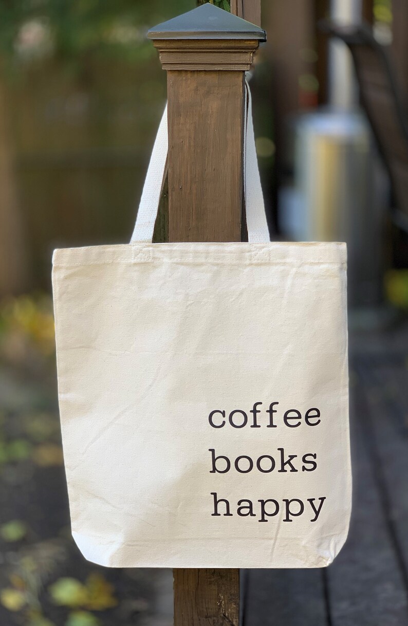 May include: A white canvas tote bag with black text that reads "coffee books happy".