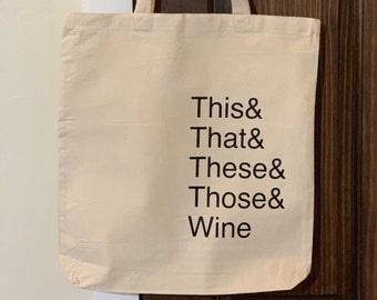 May include: A beige canvas tote bag with black text that reads "This & That & These & Those & Wine".