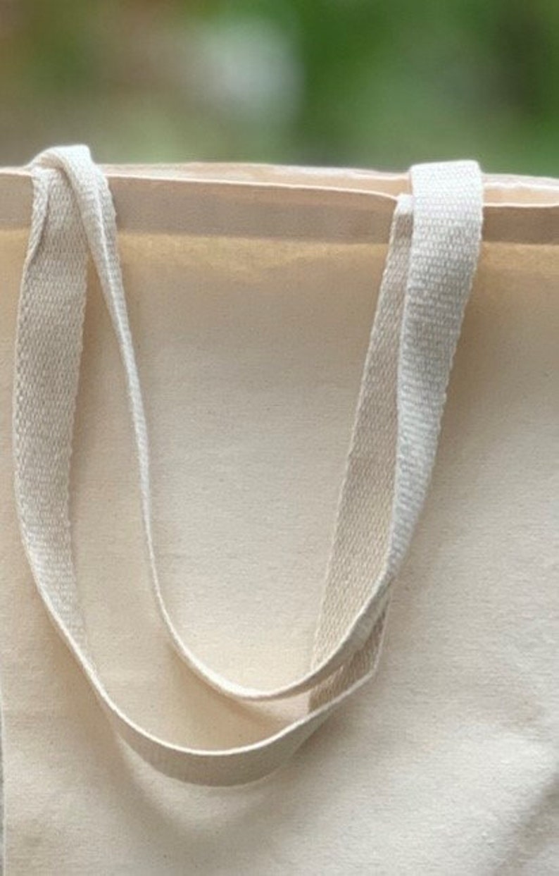 May include: A plain white canvas tote bag with two long, cream-colored straps.