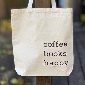 May include: A white canvas tote bag with the text "coffee books happy" printed in black.