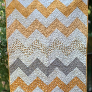 May include: A yellow, gray, and white chevron baby quilt with a small-scale floral print. The quilt is quilted with a swirl pattern.