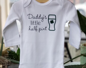 May include: White long-sleeve baby onesie with black text that reads "Daddy's little half pint" and a green shamrock inside a green beer glass.