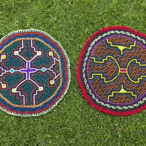 May include: Two round, hand-stitched textile pieces with intricate geometric designs. One features a dark green background with white, red, blue, and yellow patterns. The other has a brown background with orange, yellow, and purple designs, both with a red border.