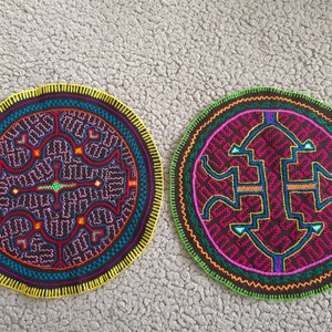 Op de afbeelding: Twee ronde, geborduurde patches met ingewikkelde geometrische ontwerpen. Eén heeft een gele rand, de andere een groene rand. Beide hebben een donkere achtergrond met kleurrijke steken in rood, blauw en roze.