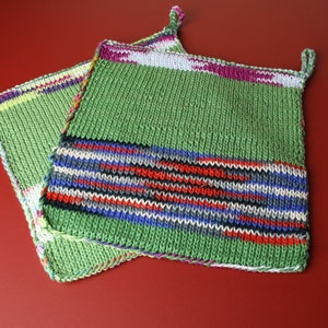 Può includere: Due presine da forno in maglia verde con strisce colorate. Una presina ha un anello per appenderla.