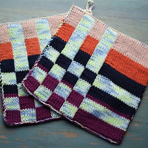 Può includere: Due presine da forno a maglia con un motivo a scacchi in tonalità di arancione, rosa, viola, verde, blu e nero.