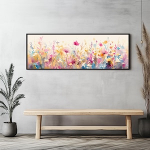 May include: A long, horizontal watercolour painting of a field of pink, yellow, and blue wildflowers. The painting is framed in a black frame and hangs on a grey wall.