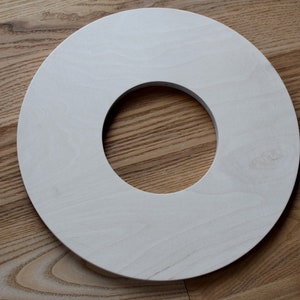 May include: A white wooden ring with a hole in the center. The ring is on a wooden surface.