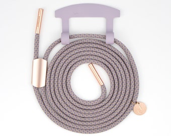 Op de afbeelding: Een paarse en beige veters met een roségouden aglet en een kleine roségouden bedel met de letter J. De veters zijn opgerold en om een ​​paarse plastic haak gewikkeld.