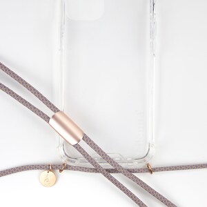 May include: A clear phone case with a gold accent and a gray and beige phone strap with a gold charm.