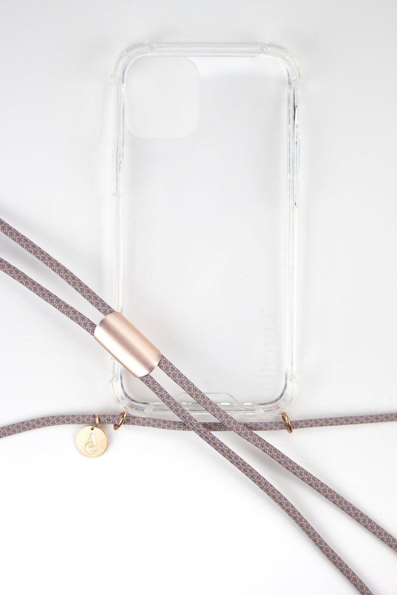 May include: A clear phone case with a gold accent and a gray and beige phone strap with a gold charm.