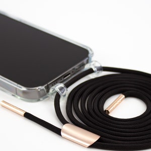 May include: A black phone case with a clear back and a black phone lanyard with gold accents. The lanyard is coiled up and the phone case is lying on a white surface.