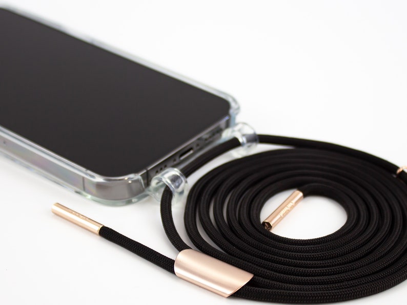 May include: A black phone case with a clear back and a black phone lanyard with gold accents. The lanyard is coiled up and the phone case is lying on a white surface.