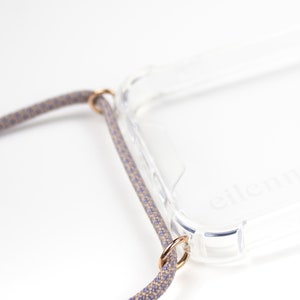 May include: A clear phone case with a gray and beige braided strap attached to the case with gold rings. The case has the word "eleni" printed on the back.
