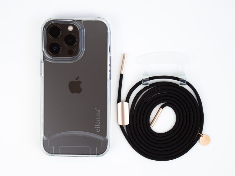 May include: A clear phone case with a black phone inside. The phone has a triple lens camera and the Apple logo on the back. The case has the word "eilenna" printed on the back. A black phone strap with gold accents is included.