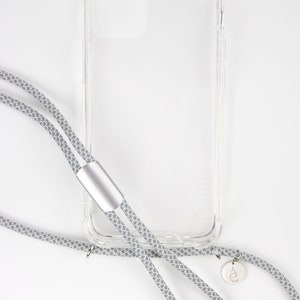 May include: A clear phone case with a gray and white patterned phone strap. The strap has a silver metal clasp and a small silver charm with a logo.