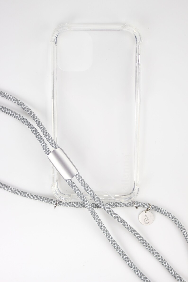 May include: A clear phone case with a gray and white patterned phone strap. The strap has a silver metal clasp and a small silver charm with a logo.