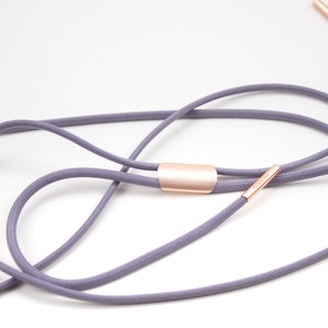 Puede incluir: Un cord&oacute;n gris con detalles met&aacute;licos de color oro rosa. El cord&oacute;n est&aacute; anudado y atado con un cierre met&aacute;lico de color oro rosa.