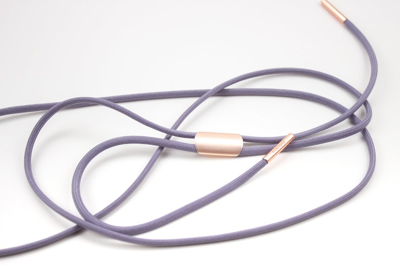 Puede incluir: Un cord&oacute;n gris con detalles met&aacute;licos de color oro rosa. El cord&oacute;n est&aacute; anudado y atado con un cierre met&aacute;lico de color oro rosa.