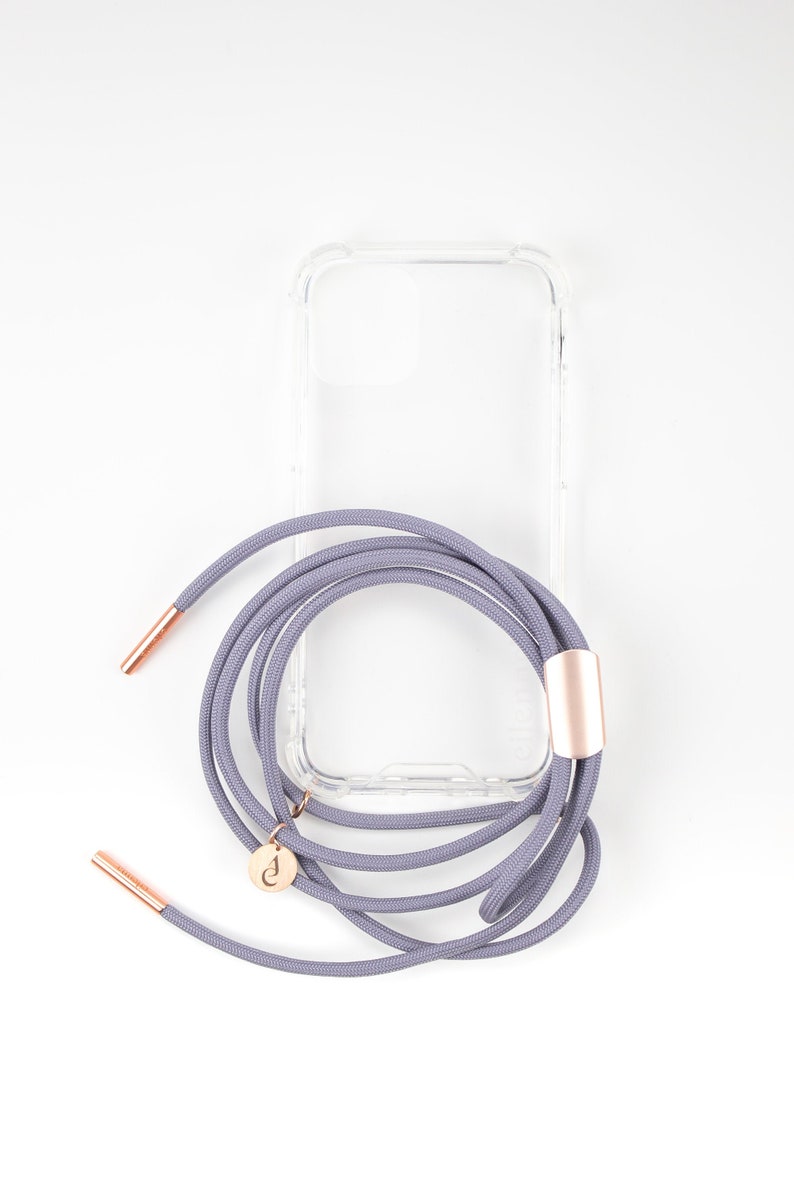 Puede incluir: Una funda de tel&eacute;fono transparente con una correa de tel&eacute;fono gris adjunta. La correa tiene un acento dorado y un peque&ntilde;o dije dorado.