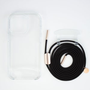 May include: A clear phone case with a black phone strap and gold accents. The strap is coiled and has a gold clasp.