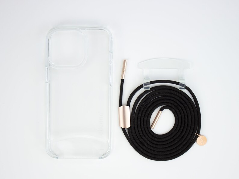 May include: A clear phone case with a black phone strap and gold accents. The strap is coiled and has a gold clasp.