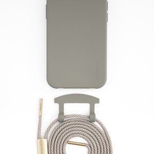 May include: A sage green phone case with a matching strap and attachment hardware. The strap is a neutral color with a repeating pattern. The hardware is gold-colored. The brand name is printed on the case and strap.