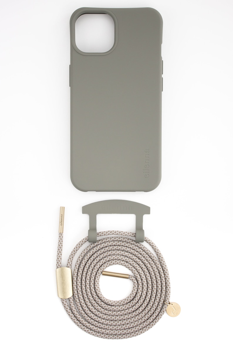 May include: A sage green phone case with a matching strap and attachment hardware. The strap is a neutral color with a repeating pattern. The hardware is gold-colored. The brand name is printed on the case and strap.