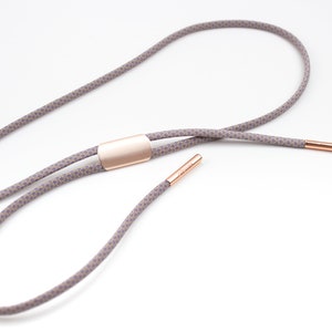 May include: A gray and white patterned lanyard with a rose gold metal slider and end caps.