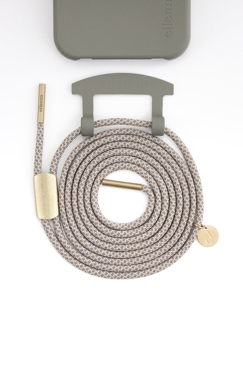 May include: A phone case and lanyard set in neutral tones. The olive green case and holder are paired with a beige and brown patterned rope lanyard. The lanyard features gold-colored metal accents and a small charm.