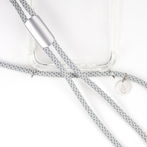 May include: A gray and white patterned phone strap with a silver accent and a small silver charm. The strap is attached to a clear phone case.