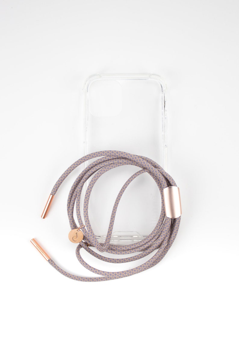 May include: A clear phone case with a patterned phone strap. The strap is a light brown color with a blue pattern and has rose gold accents.