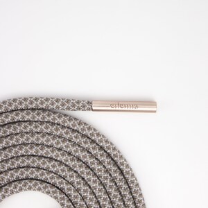 May include: Coiled gray and white patterned shoelace with a metallic aglet. The aglet has the brand name "eilenna" printed on it. The shoelace is made of a durable, woven material.