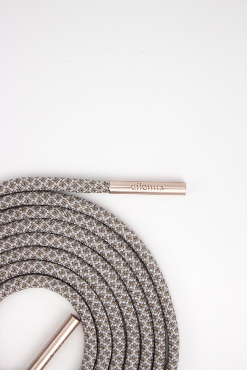 May include: Coiled gray and white patterned shoelace with a metallic aglet. The aglet has the brand name "eilenna" printed on it. The shoelace is made of a durable, woven material.
