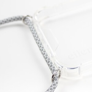 May include: A clear phone case with a gray braided strap attached to the case with metal rings.