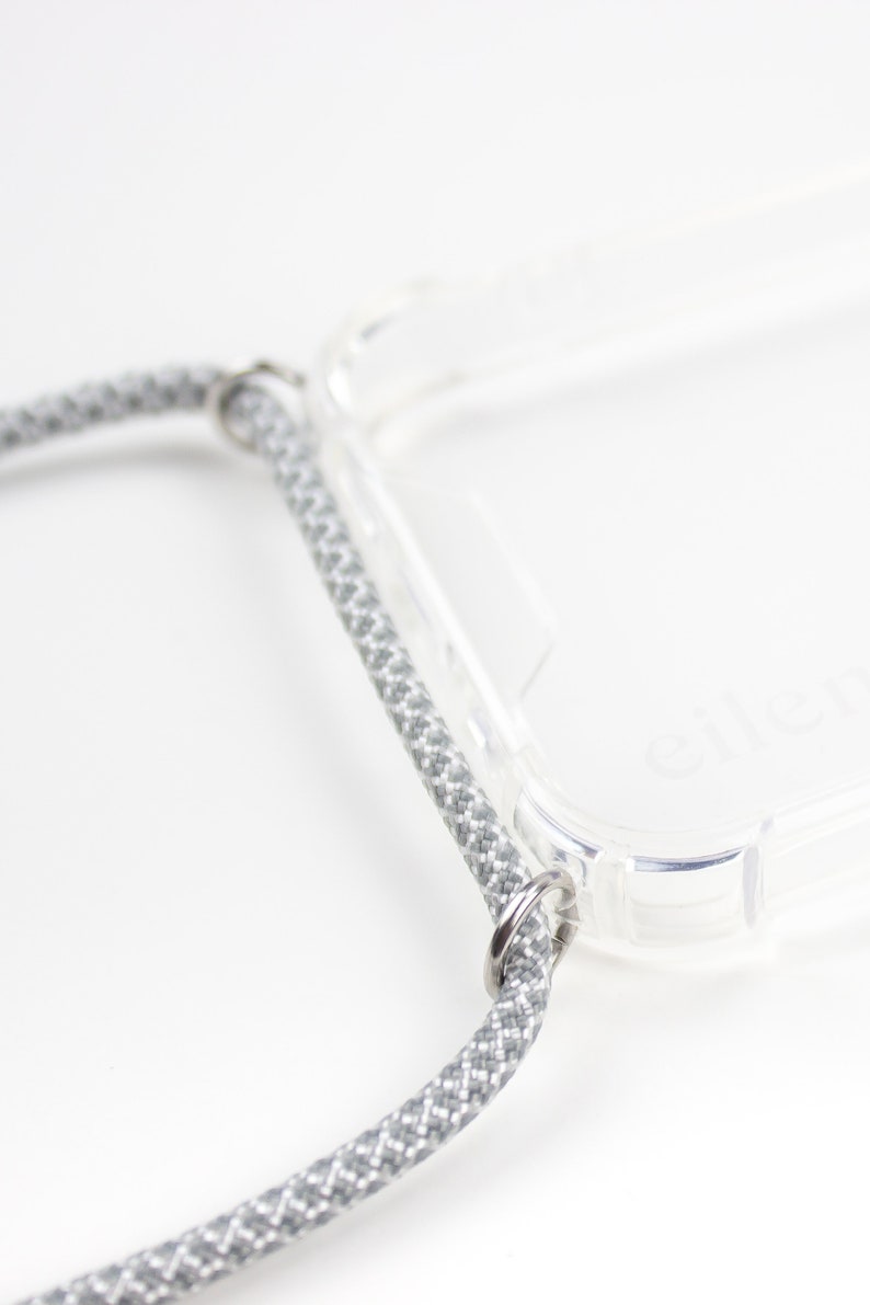 May include: A clear phone case with a gray braided strap attached to the case with metal rings.