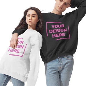 May include: Two people wearing black and white sweatshirts with the text "YOUR DESIGN HERE" printed in pink. The sweatshirts are a classic crew neck style.