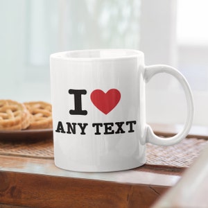 May include: White ceramic mug with a black "I love" design and a red heart. The text "ANY TEXT" is printed below the heart.