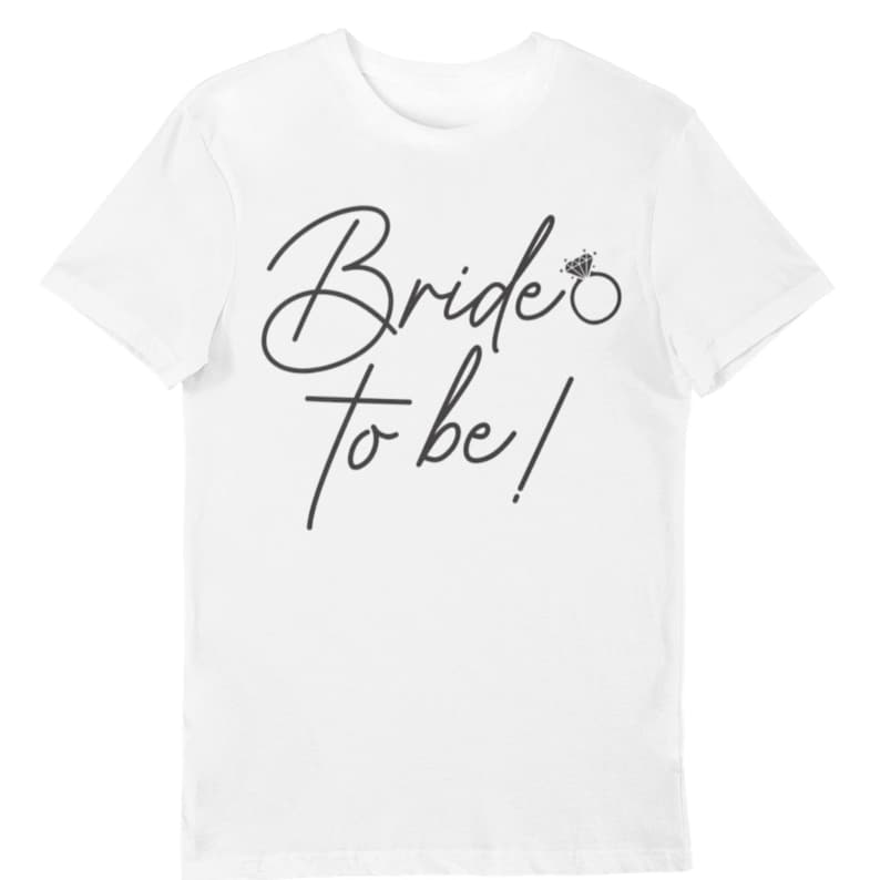 May include: White t-shirt with the text "Bride to be!" in a stylish, cursive font. A diamond ring graphic is next to the text. The shirt is a short-sleeved, crew neck style.