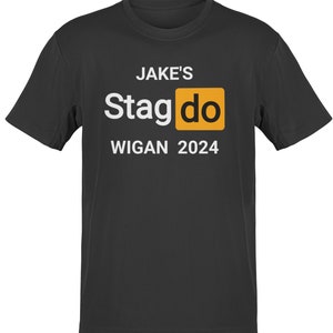 May include: Black t-shirt with white text that reads "JAKE'S Stagdo WIGAN 2024". The word "Stagdo" is in a yellow box.