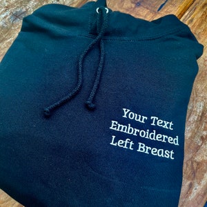 May include: Black hooded sweatshirt with the text "Your Text Embroidered Left Breast" in white embroidery on the left side.