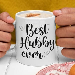 May include: White ceramic coffee mug with black text that reads "Best Hubby ever."  Two small grey hearts are on either side of the text.