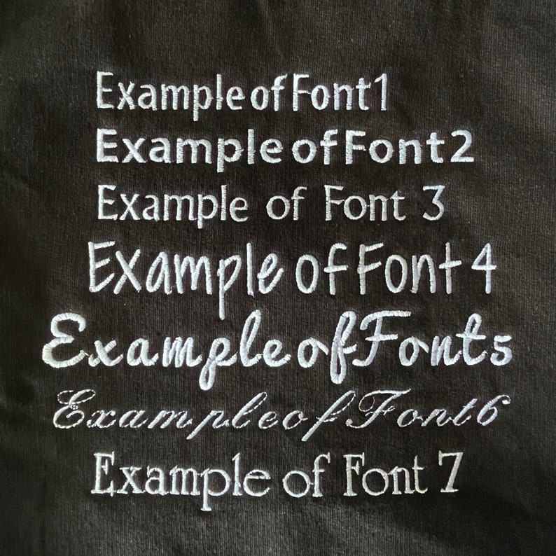May include: A close-up of a black fabric with seven examples of different fonts in white embroidery. The text reads: "Example of Font 1", "Example of Font 2", "Example of Font 3", "Example of Font 4", "Example of Fonts", "Example of Font 6", and "Example of Font 7".