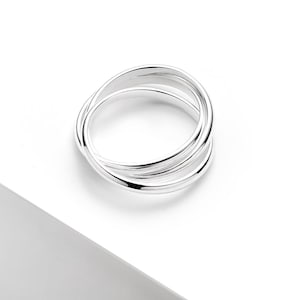 May include: A silver ring with a distinctive design. The ring has three intertwined bands, giving it a modern and elegant appearance. The polished metal reflects light, emphasising the ring's smooth, curved lines. A stylish accessory.