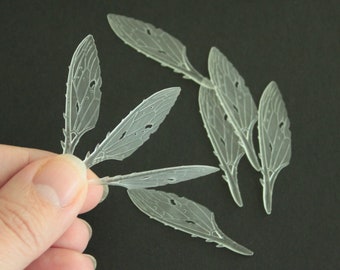 May include: A set of six translucent, white, insect wings with delicate veining. The wings are made of a thin, flexible material and have a slightly iridescent sheen.