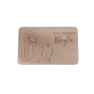 May include: A wooden cutting board with a laser-engraved design of a bunny rabbit sitting under a flower. The text "Hier kr&uuml;melt Mayla" is engraved on the board.