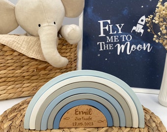 May include: A wooden rainbow stacking toy in shades of blue and gray with a personalized wooden plaque that reads "Emil Zur Taufe 28.05.2023".