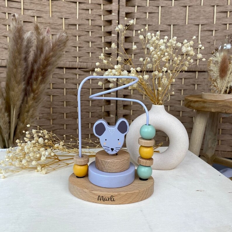 May include: A wooden toy with a mouse face and a wire maze. The toy has a stack of colorful beads and a base with the word "Marli" on it.