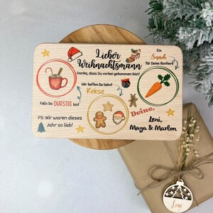 May include: A wooden sign with a Christmas theme. It says "Lieber Weihnachtsmann" and has a carrot, cookies, and a mug of hot chocolate. It also says "Danke, dass Du vorbei gekommen bist!" and "Wir hoffen Du Liebst Kekse". The sign is signed "Deine, Leni, Maya & Marlon".